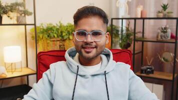 Portrait of happy calm Indian man at home chair smiling friendly, glad expression looking away dreaming resting, relaxation feel satisfied good news, celebrate win. Arabian young guy in living room video