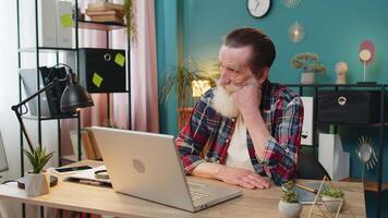 Thoughtful concerned Caucasian senior man looking away thinking solving problem with laptop at desk in home office. Serious grandpa freelancer search for inspiration make decision feel lack of ideas. video