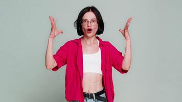Young woman rolls eyes and throws arms outward in dramatic gesture, showing mind blown reaction to shock or mental overload. Caucasian girl exaggerates emotional disbelief, isolated on gray background video