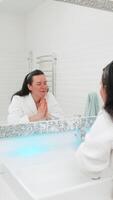 Mature middle-aged woman energetically washing face with cold water, feeling instant refreshment and vitality. Her face lights up with a fresh, open look, full of energy to start the day strong video