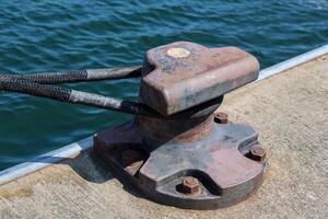 Mooring bollard securing rope on a cement pier by the sea photo