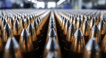 Rows of polished copper bullet projectiles with silver tips in a factory setting photo