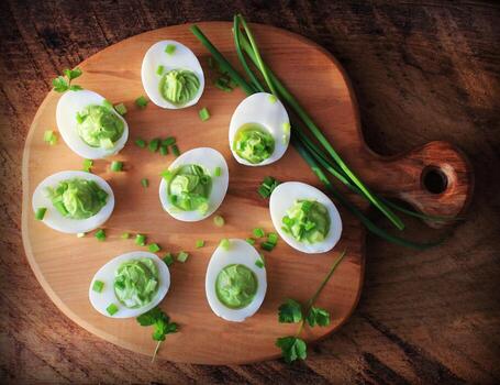 Stuffed deviled eggs appetizer with avocado and leek on cutting board. Top view photo