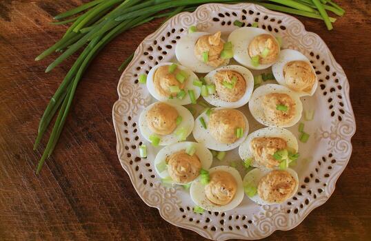 Deviled eggs with cod livers with leek on white plate. Rustic wooden table photo