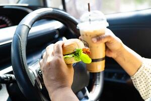 Asian woman driver hold and eat hamburger and cold coffee in car. photo