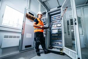 Adult electrician builder engineer testing and screwing equipment in fuse box and repairing of electricity power station photo