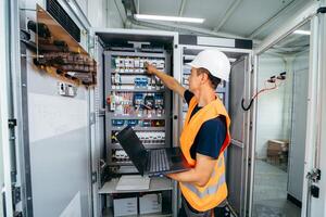 Adult electrician builder engineer testing and screwing equipment in fuse box and repairing of modern electricity power station. Automatic control cabinet. photo