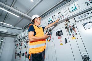 Adult electrician builder engineer testing and screwing equipment in fuse box and repairing modern electricity power station using data from the tablet. Automatic control cabinet photo