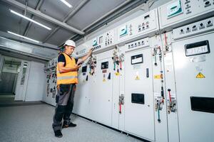 Adult electrician builder engineer testing and screwing equipment in fuse box and repairing of modern electricity power station using data from the tablet photo