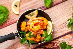 Juicy fried shrimps with lemon wedges in a frying pan on a wooden photo