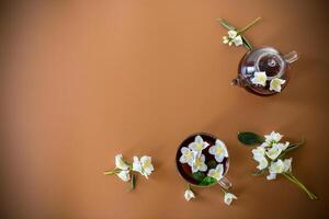 Tea composition with green tea and jasmine flowers on a brown background photo