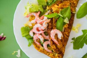 Delicious omelette with shrimps and fresh greens on top, on a green background photo