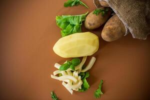 Nutritious potatoes whole, peeled and sliced on a brown background photo