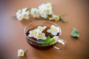 Glass teapot with jasmine and green tea isolated on a brown background photo