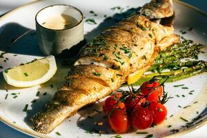 Grilled whole fish with asparagus, lemon wedge, cherry tomatoes, and sauce on plate photo