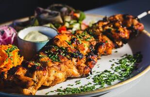 Grilled chicken skewers with fresh salad and sauce on plate photo