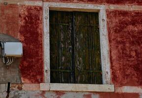 Rustic aged window with weathered green shutters on red textured wall photo