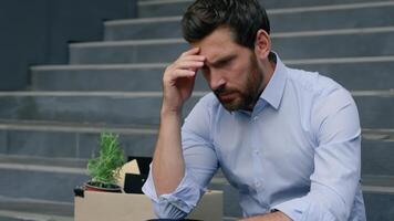 Close up depressed Caucasian middle aged business man lost job pensive holding head frustrated emotion sitting stairs near office building with dismissal box businessman male suffering unemployment photo