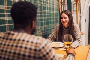 A mixed race couple enjoys casual lunch, smiling and talking while seated at a stylish restaurant table. photo