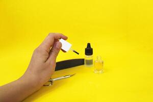 Manicure at home. On a yellow background there is cuticle oil and varnish, next to it there are scissors and a nail file. In a woman's hand there is a varnish brush photo