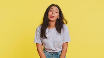Playful Indian young woman showing tongue making faces at camera, fooling around, joking, aping with silly face, teasing, bullying, abuse. Cheerful funny Arabian girl isolated on yellow background video