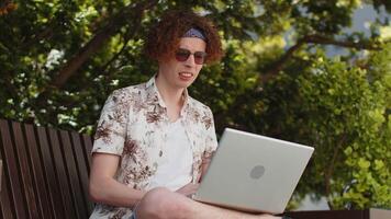Young man tourist using laptop computer typing browsing, loses becoming surprised sudden lottery results, bad news, fortune loss, fail. Angry guy sits on bench in urban city outdoors. Town lifestyles. video