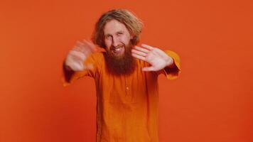 Young Caucasian man smiling friendly at camera, waving hands gesturing hello greeting or goodbye welcoming with invitation hospitable expression. Redhead guy isolated on orange studio background video