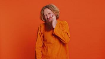 Dental problems. Caucasian man touching cheek closing eyes with expression of terrible suffer from painful toothache sensitive teeth cavities. Redhead young guy isolated on orange studio background video