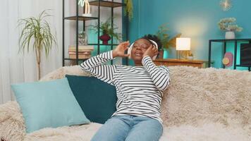African American woman relaxing on sofa with closed eyes, taking deep breaths, listening to calm music through headphones, meditation indoors. Peaceful mood, tranquility, serene environment at home video