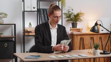 Caucasian successful businessman in formal suit sitting at workplace in home office counting money dollars salary holding stack of dollars, analyzes budget finances. Young freelancer sitting at table. video