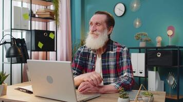 Thoughtful concerned Caucasian senior man working on laptop computer looking away thinking solving problem at home office. Grandpa freelancer search for inspiration make decision feel lack of ideas video