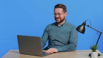 Happy man closing laptop pc after finishing successful work relaxing. E-learning, browsing internet on notebook computer. Guy freelancer working online remote job isolated on blue background indoors video