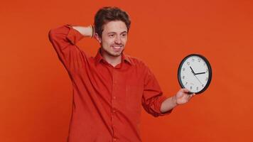 Caucasian man with anxiety checking time on clock, running late to work, being in delay, deadline. Young guy looking at hour, minutes, worrying to be punctual isolated on studio orange background video