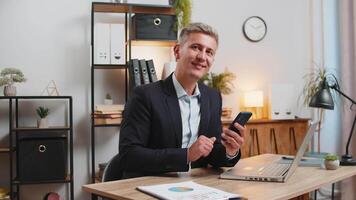 Confident young businessman using smartphone application online pointing showing like thumbs up gesture, remote distance job working from office. Handsome guy freelancer looking at camera. Advertising video