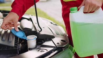 Close-up of service worker man driver pouring non freezing windshield cleaning glass washer fluid into hood car tank from bottle. Winter or summer fluid green windscreen liquid glass window cleaner video