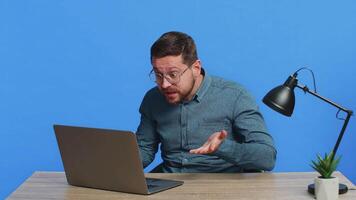 Man arguing while talking on laptop conversation by webcam, quarrels, expresses a problem with employees. Screaming shouting by megaphone loudspeaker. Young adult guy isolated on blue background video