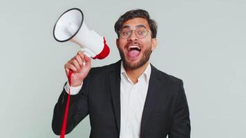 Indian businessman talking with megaphone, proclaiming news, loudly announcing advertisement discounts sale, using loudspeaker to shout speech. Happy Arabian man guy isolated on studio gray background video
