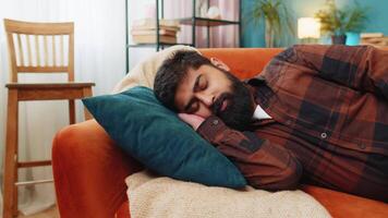 Tired Indian young man lying down in bed taking a rest. Carefree peaceful guy napping, falling asleep on comfortable sofa with pillows at home living room. Closes his eyes enjoy daytime nap alone video