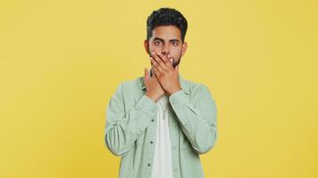 I will not say anything. Frightened Indian man closing mouth with hands, looking intimidated scared at camera gestures no, refusing to tell terrible secret unbelievable truth. Guy on yellow background video