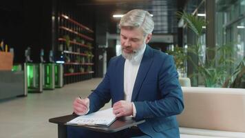 Caucasian middle-aged businessman working with documents, analyzing information, reading papers prepare financial report. Happy male entrepreneur in suit analyzing graph documents in office lobby. video