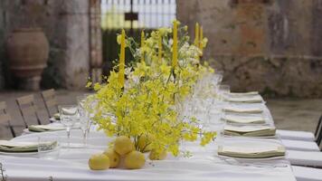 Elegant yellow table setting with lemons and orchids in a rustic courtyard. Action video