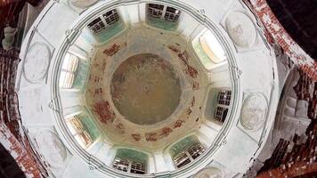 View from below dome of an abandoned Christian church made of red brick and plaster. On ceiling, there are traces of destroyed fresco depicting faces of saints and Jesus Christ. video