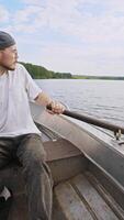 A young man, steering a boat, turns it around by using one oar to row while sailing on a lake. video