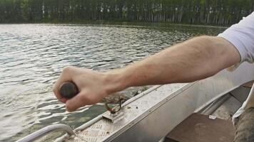 Close-up of a boatman's hand rowing through the water while sitting on a rowboat using a oarlock. behind river bank and forest. summer video