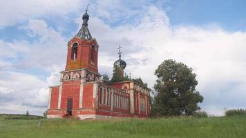 Abandoned 19th-century Christian Orthodox brick church stands in middle of field on bright summer day. Grass and trees have grown from its roof, adding to natural beauty of scene. Exterior video
