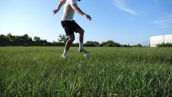 Profesional footballer in uniform shows tricks with ball while running at green field. Sportsman kicks ball during jogging at meadow on sunny day. Young man training at stadium. Freestyle football video