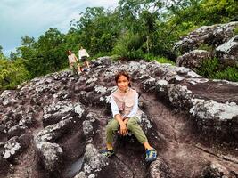 Cute girl smiles and sits down to rest while walking on a mountain, family trip in mountains. Mother and children are enjoying nature outdoors. photo