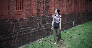High angle view shot, Relaxed woman wearing a striped shirt and green pants walking around, admiring the natural scenery and ancient brick structures, Enjoy holiday travel. video