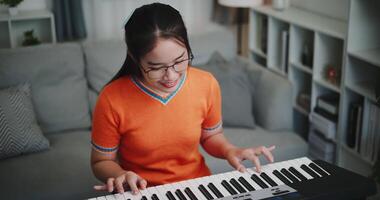 Happy woman in an orange shirt is practicing her keyboard skills intently in a living room. Enjoy favorite musical instruments video