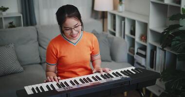 High angle view shot, Happy young woman in an orange shirt is practicing her keyboard skills intently in a living room. Enjoy favorite musical instruments video